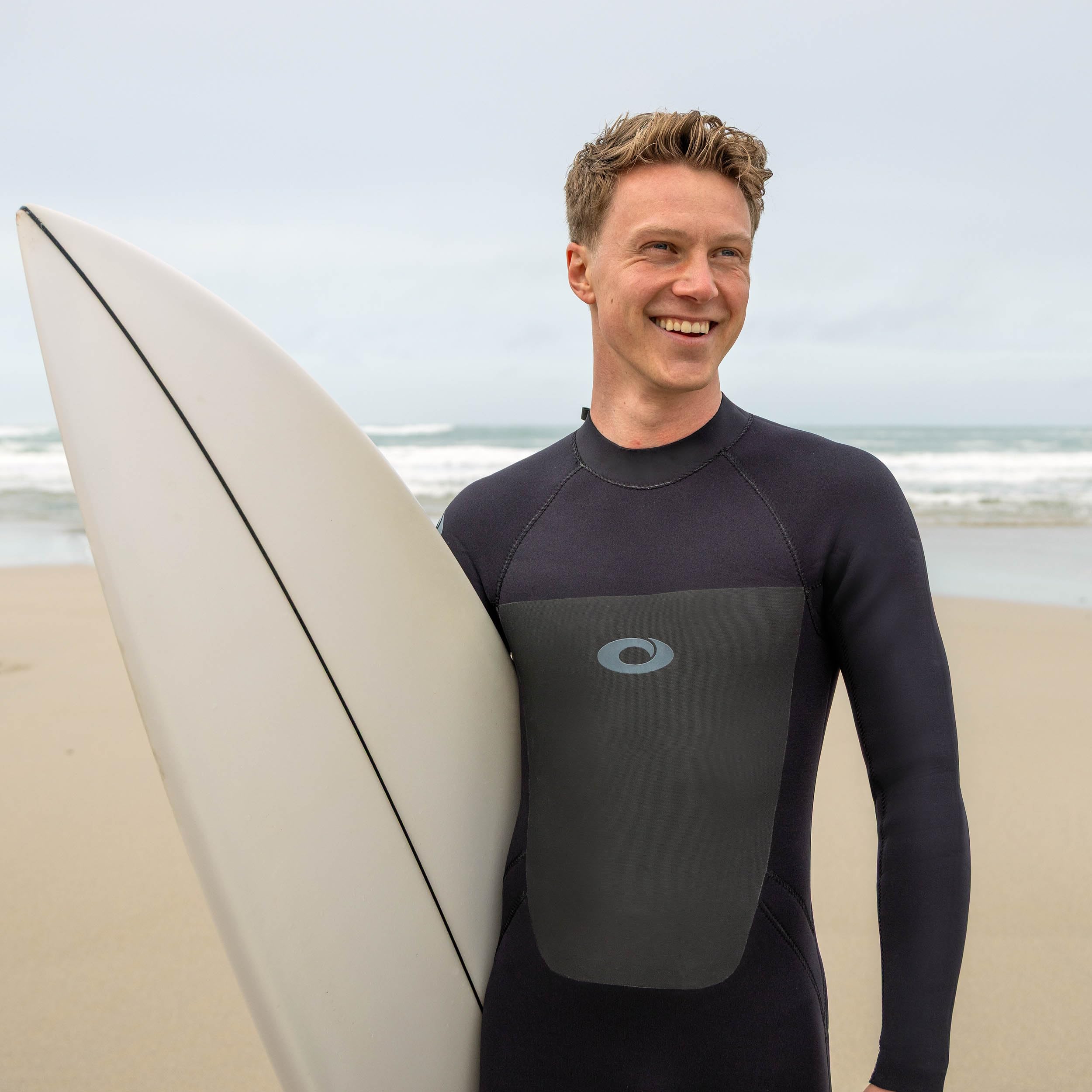 Man in a wetsuit holding a surfboard on a beach