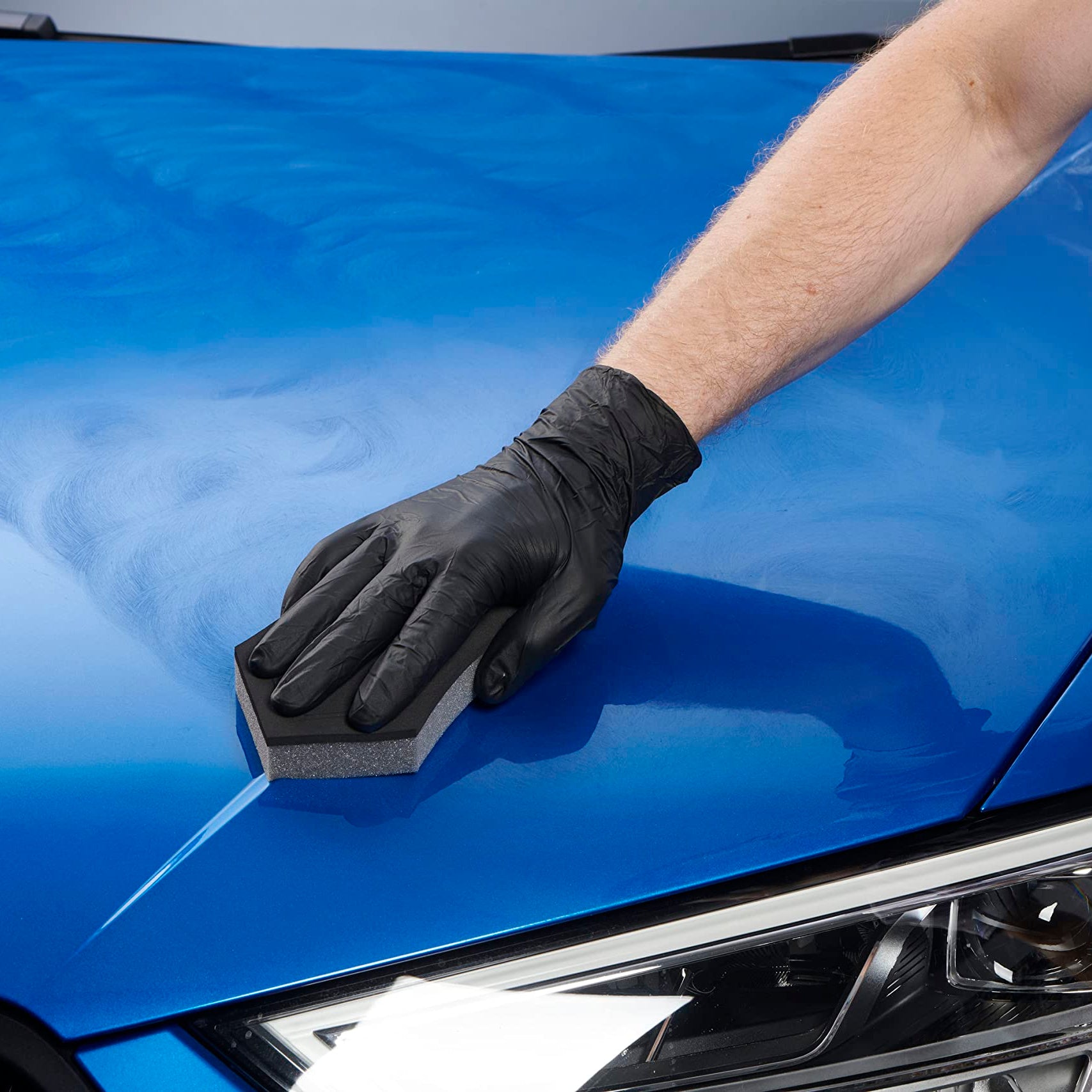 Person wearing a black glove polishing a blue car hood.
