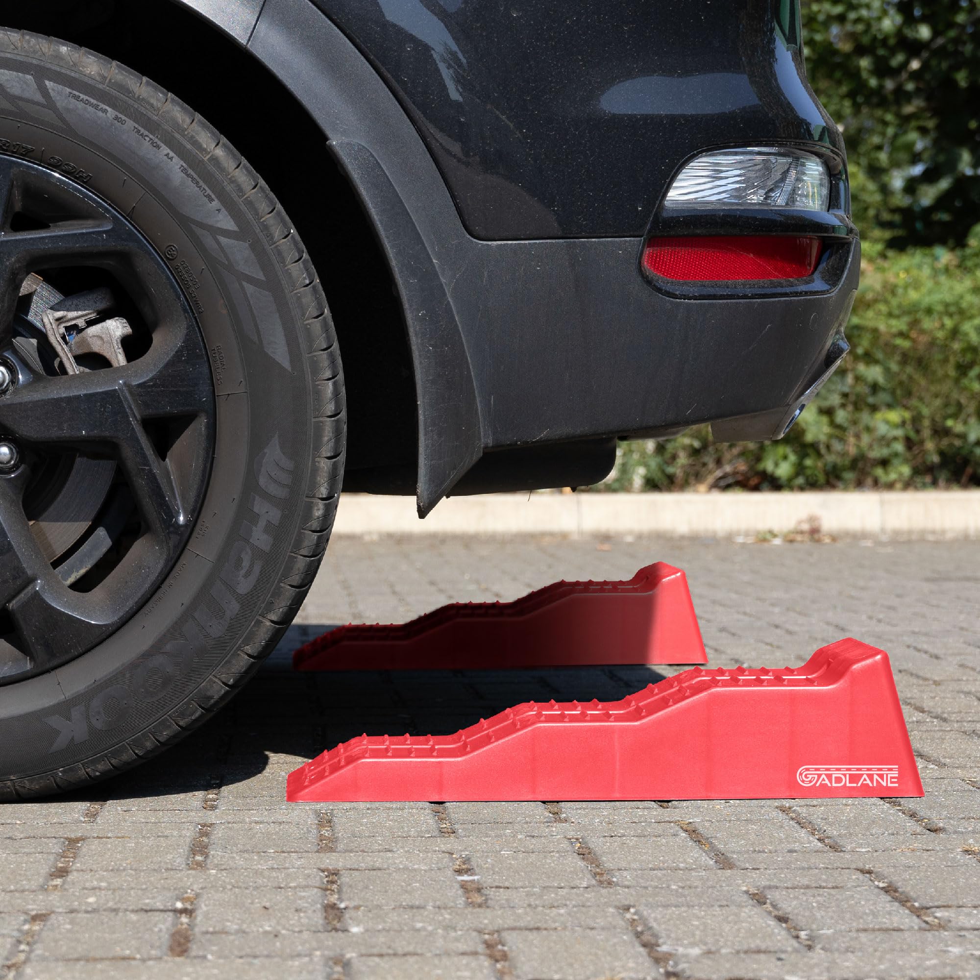 Red car jack stand under a black car on a driveway