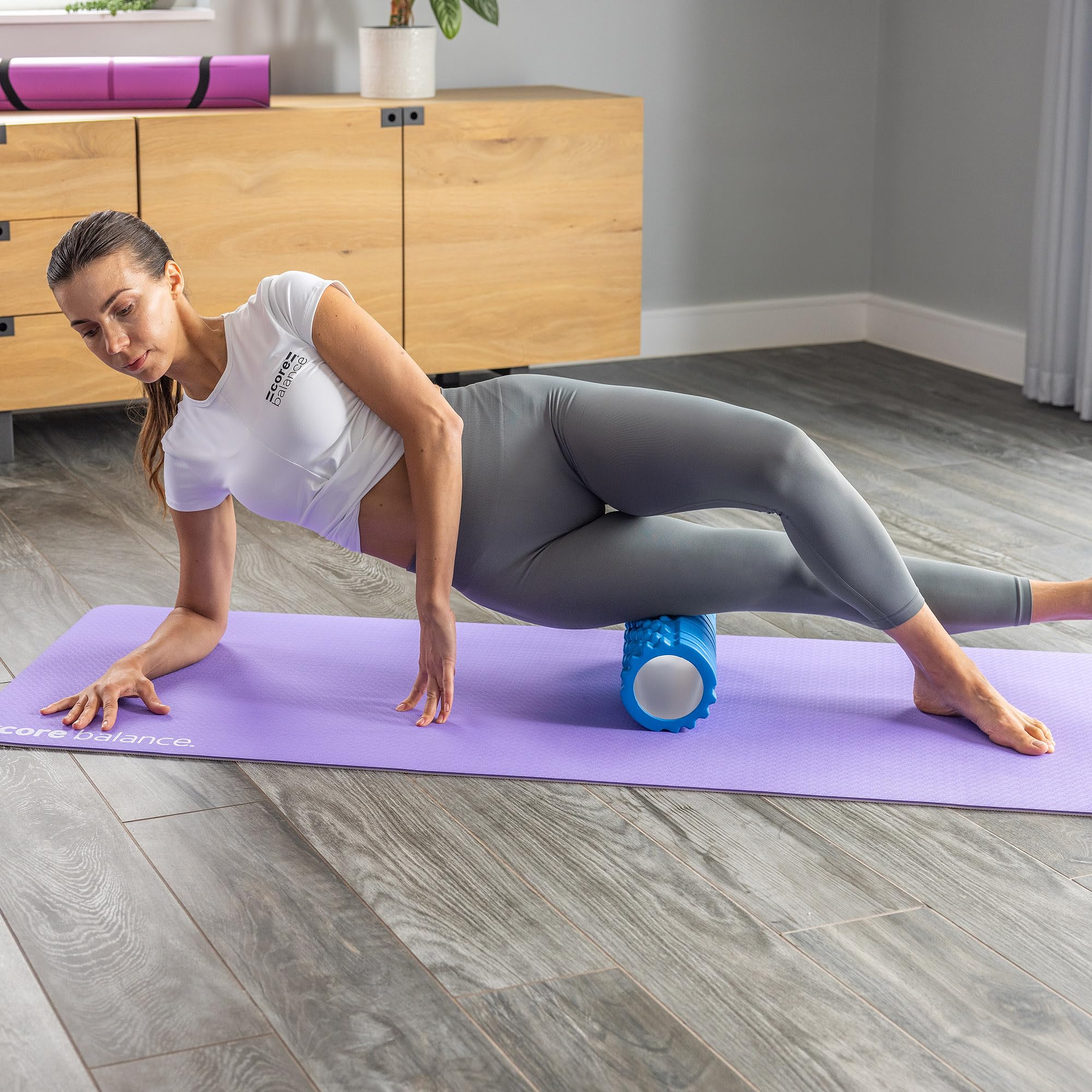 Woman using a foam roller on a purple mat in a home setting