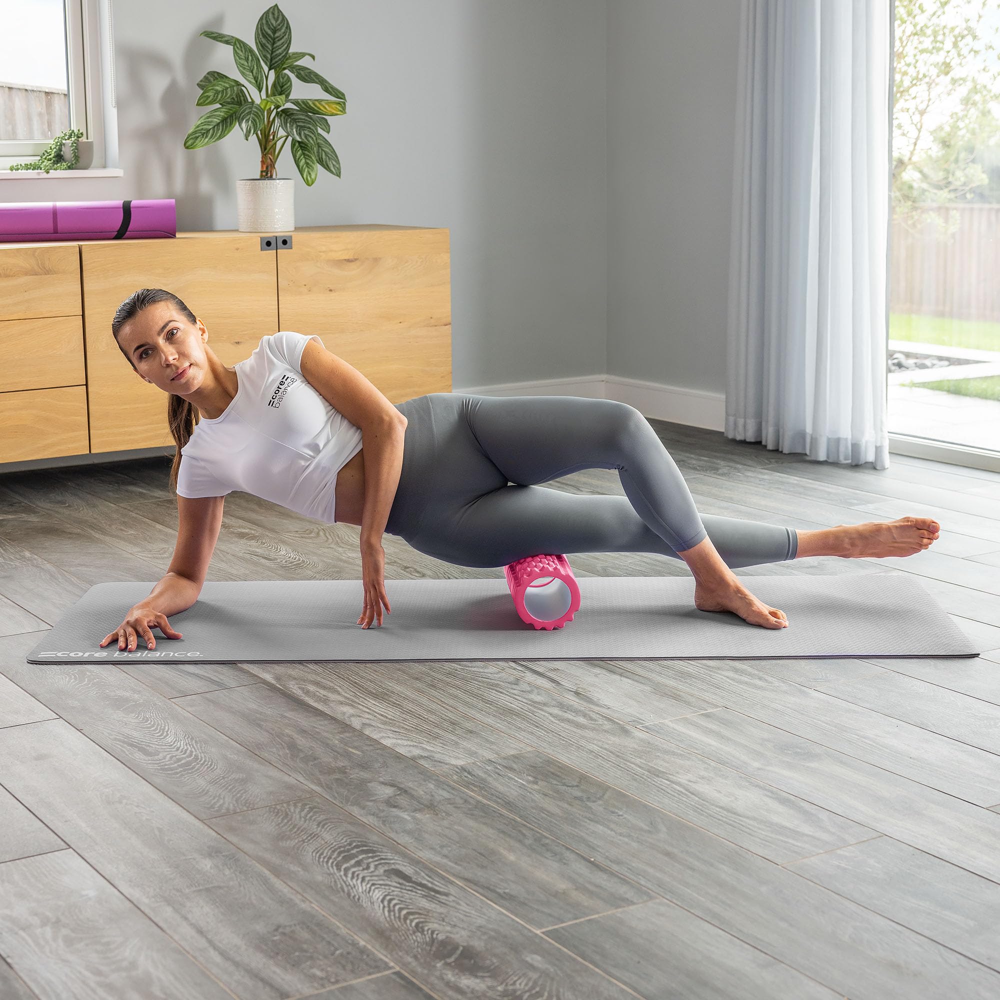 Woman exercising with a pink foam roller on a mat in a home setting