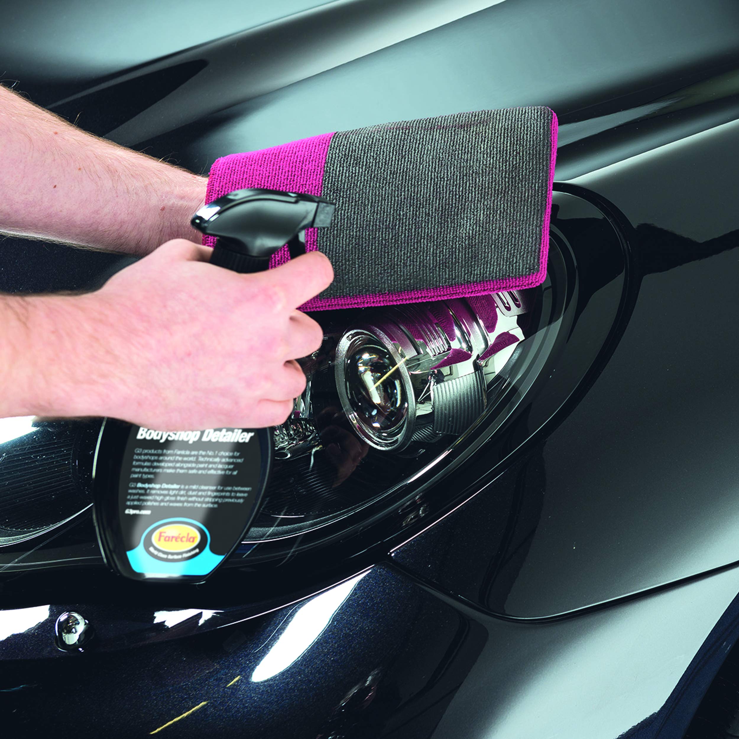 Person cleaning a car headlight with a detailing cloth and bottle of cleaner.