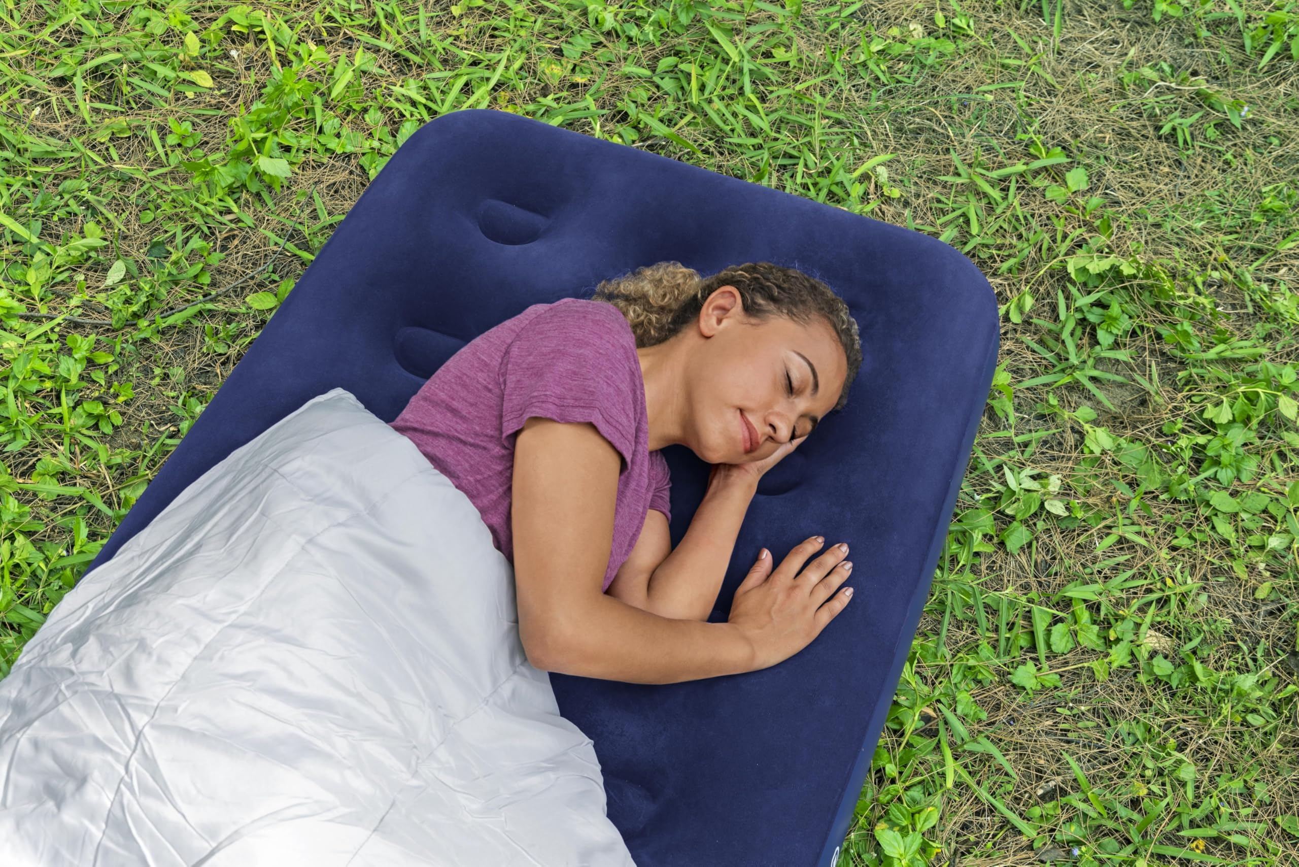 Woman sleeping on a blue inflatable camping pillow outdoors.