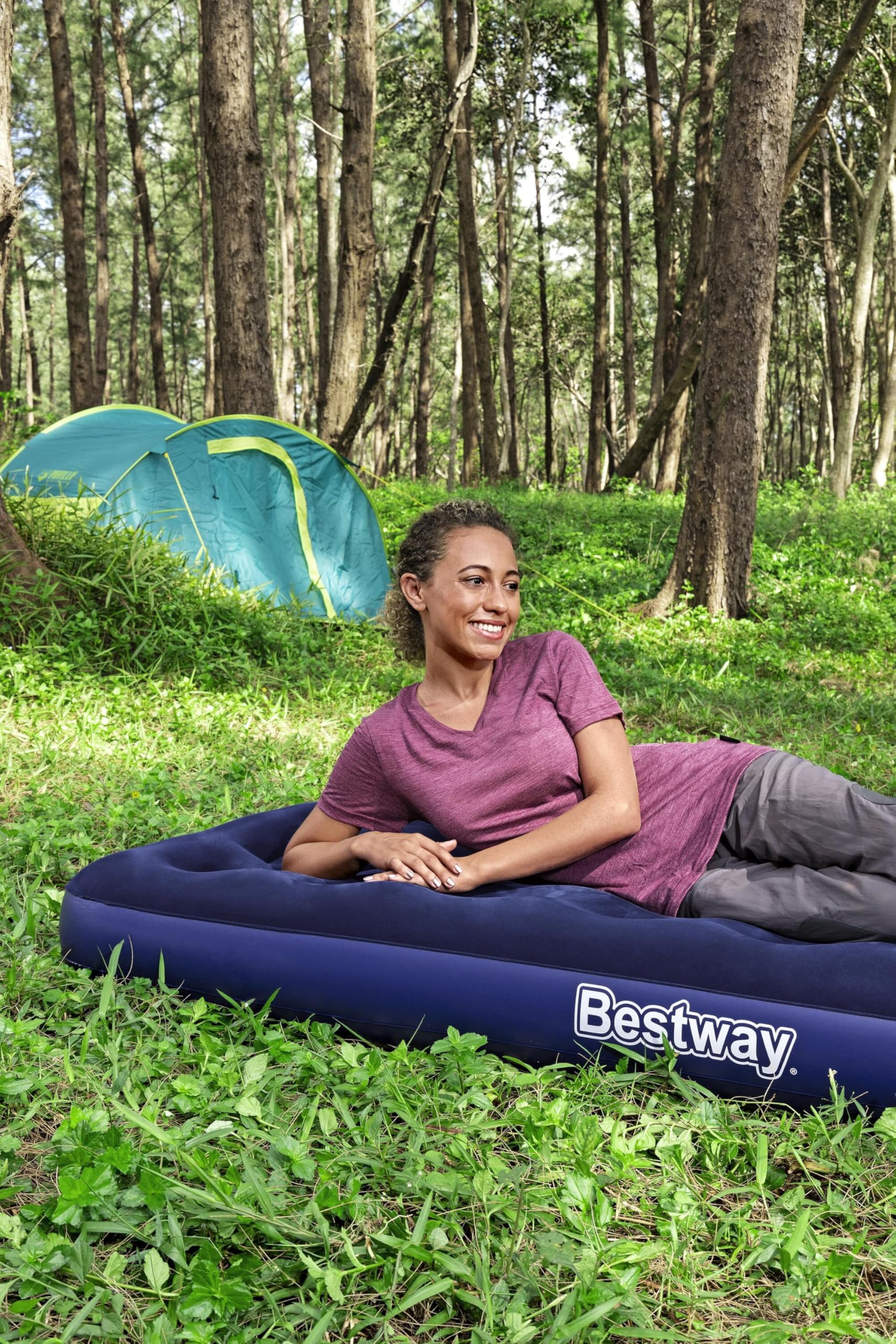 Woman lying on a Bestway inflatable mattress in a forest with a tent in the background