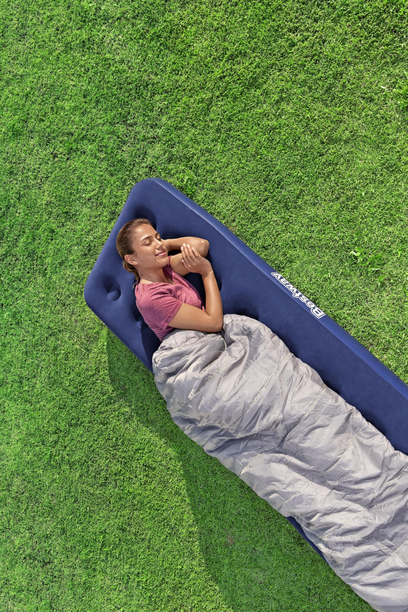 Person lying on a blue inflatable mattress with a gray sleeping bag on grass