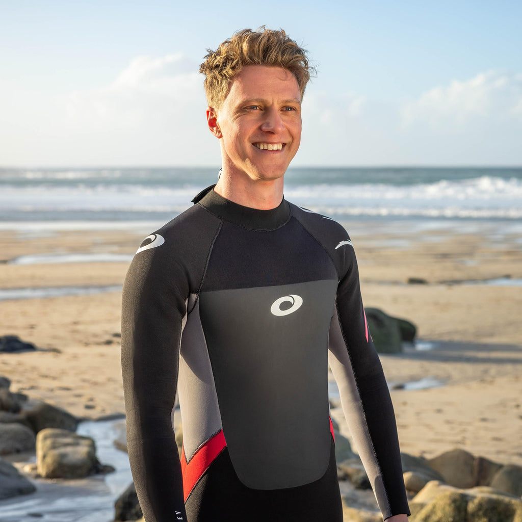 Man wearing a wetsuit on a beach with ocean and sky in the background